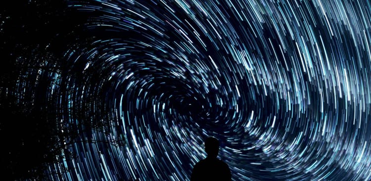 The silhouette of a person's head and shoulders in front of a sweeping solar system's analemma