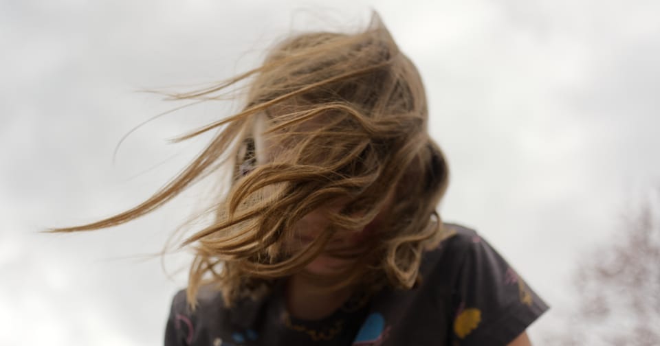 A young girl, her blonde hair blown into tendrils by the wind, face obscured
